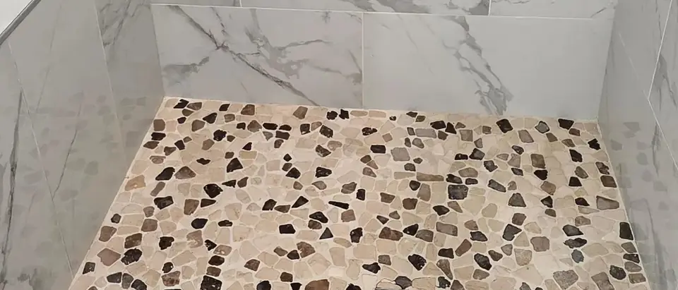 The floor and lower walls of a walk-in shower: marble-look wall tile and a pebble floor