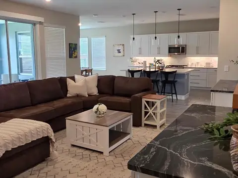 A living room with a brown sectional sofa and a white coffee table, with a kitchen island behind