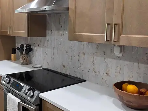 A slide-in electric range under a stainless steel hood, between white counters and wood cabinets