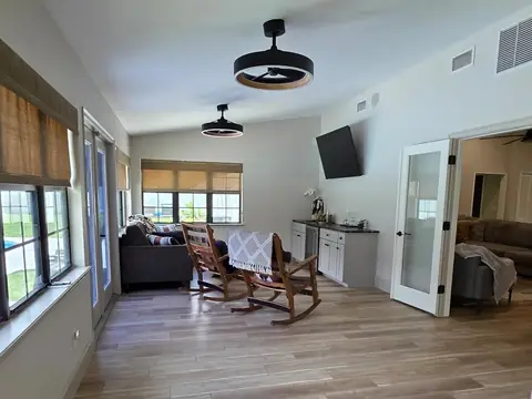 A sunroom with two wooden rocking chairs, a small bar cabinet and a wood-look tile floor