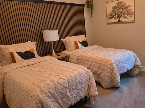 Two twin beds with cream tufted comforters in front of a wood slat wall