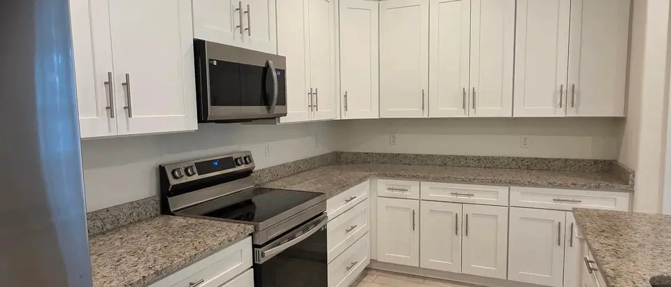 An empty kitchen with white cabinets, bare granite counters and a stainless steel range