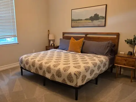 A made bed with a patterned quilt in a bedroom with vacuum lines on the carpet