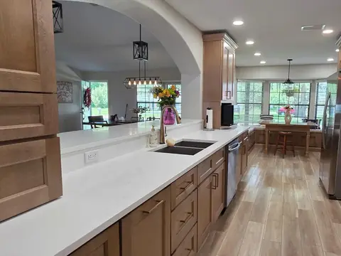 A kitchen with a long white counter, a double sink and wood cabinets