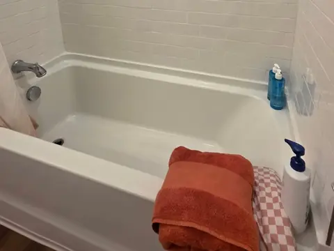 A clean white bathtub and tile wall with a folded orange towel on the rim