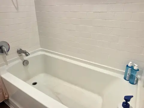 A white bathtub with water spots on the tile wall and a film on the floor of the tub