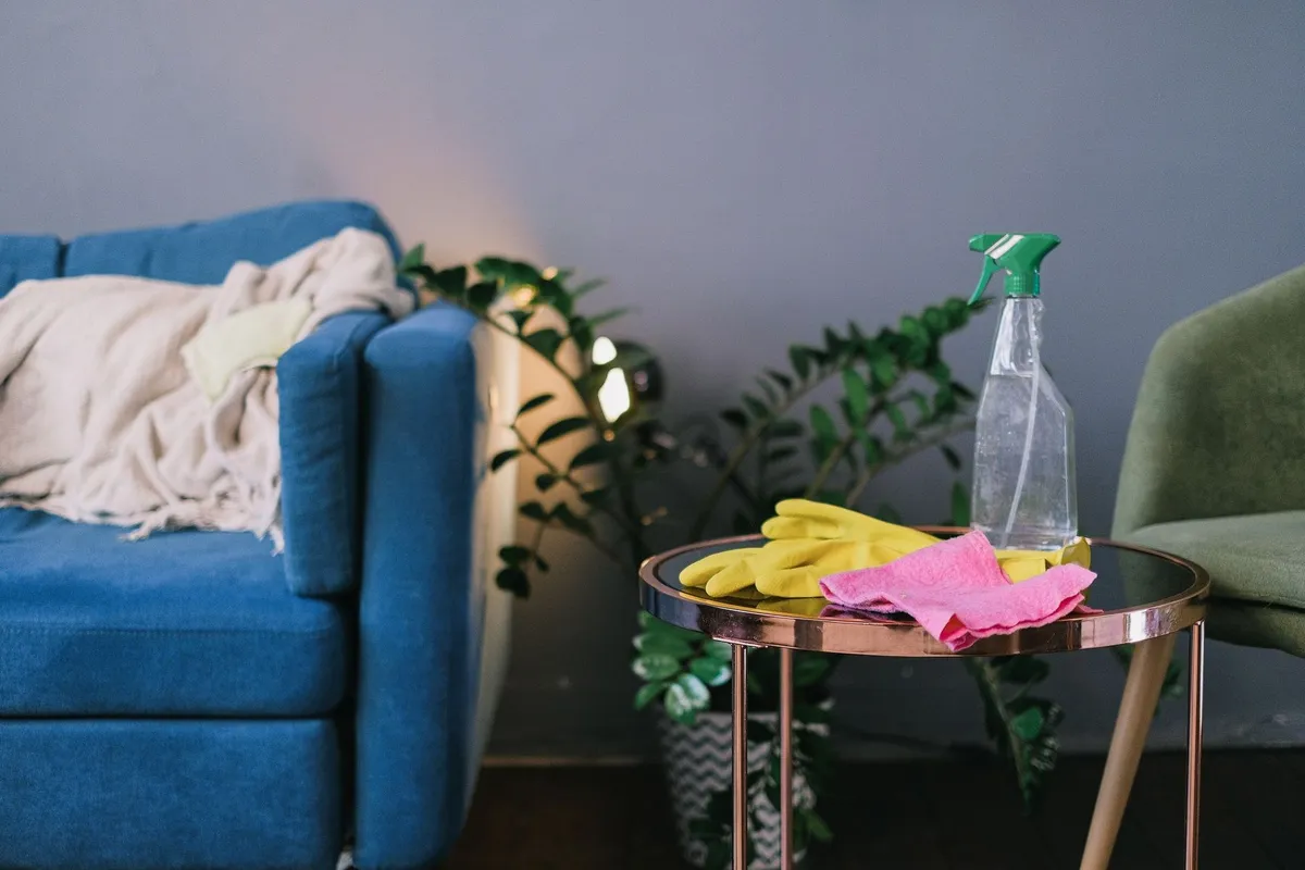 Latex gloves and spray detergent on a table in a stylish living room, highlighting cleaning needs after local events.